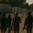 Four soldiers in tactical gear walking together with rifles in a dusty outdoor setting.